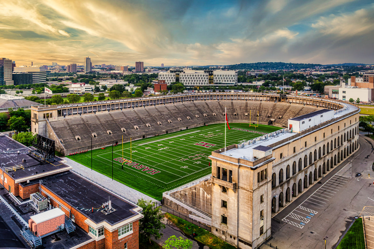 Aerial view of historic Harvard Stadium with its horseshoe-shaped concrete grandstands surrounding the Harvard Crimson football field beneath a dramatic summer sky.