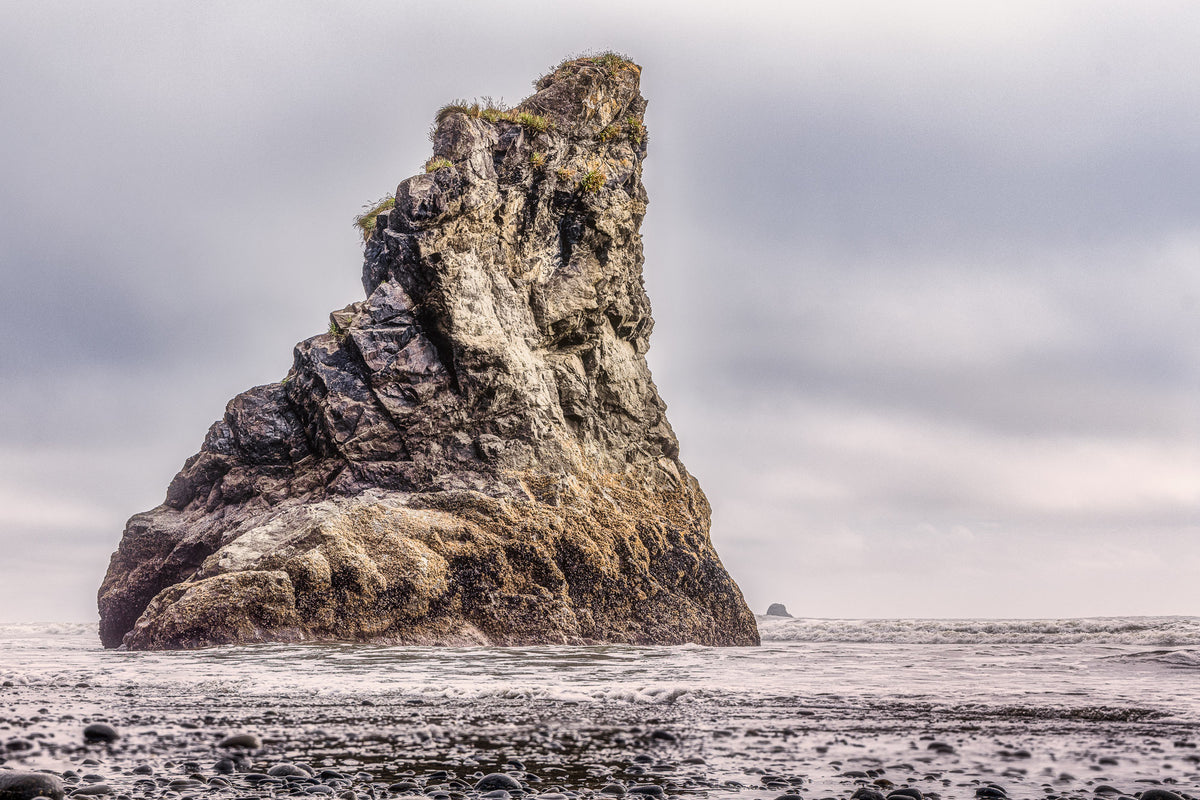 Massive rugged sea stack rising from the Pacific Ocean amid crashing waves at Ruby Beach near Olympic National Park in Washington.