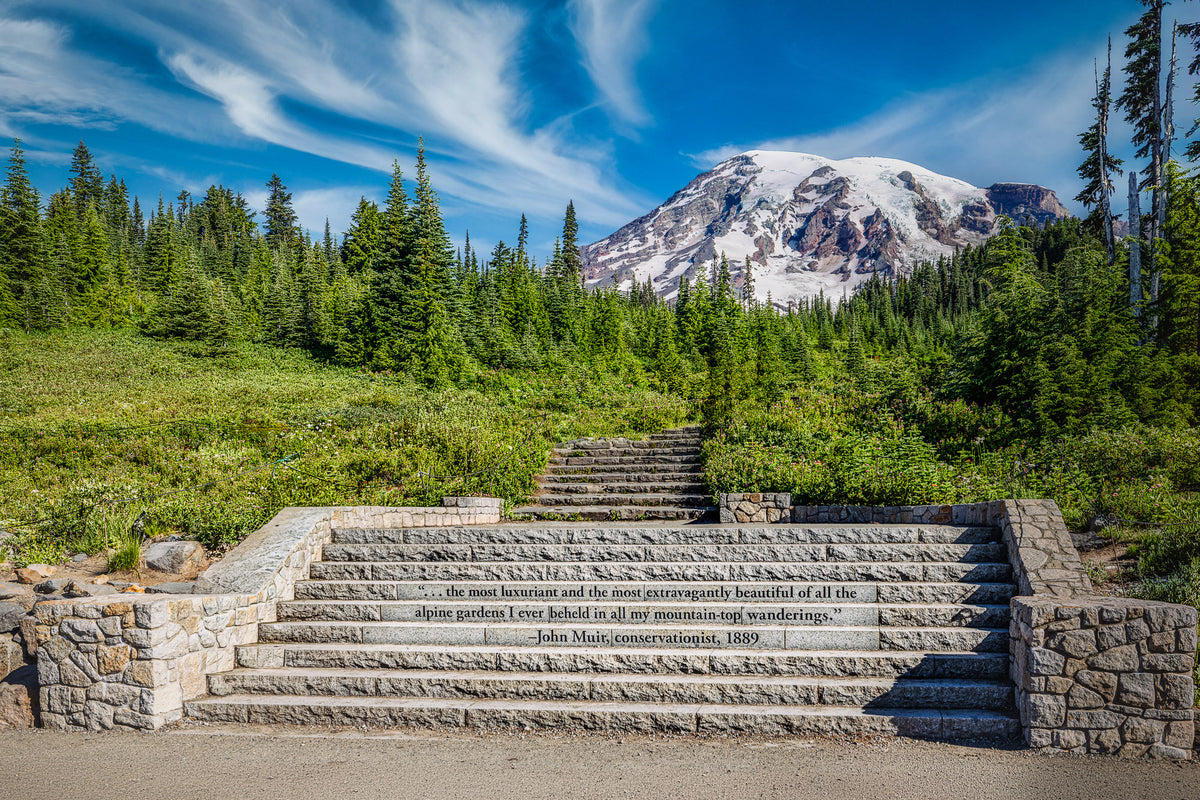 The Muir Steps at Paradise inscribed with a John Muir quotation, leading toward snow-covered Mount Rainier beneath a vivid blue sky.